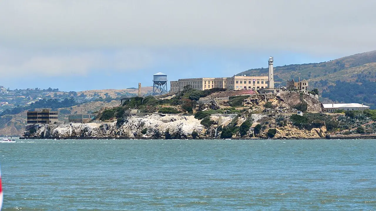Alcatraz Island seen from the water with the cellhouse, lighthouse and water tower, an American flag in the foreground