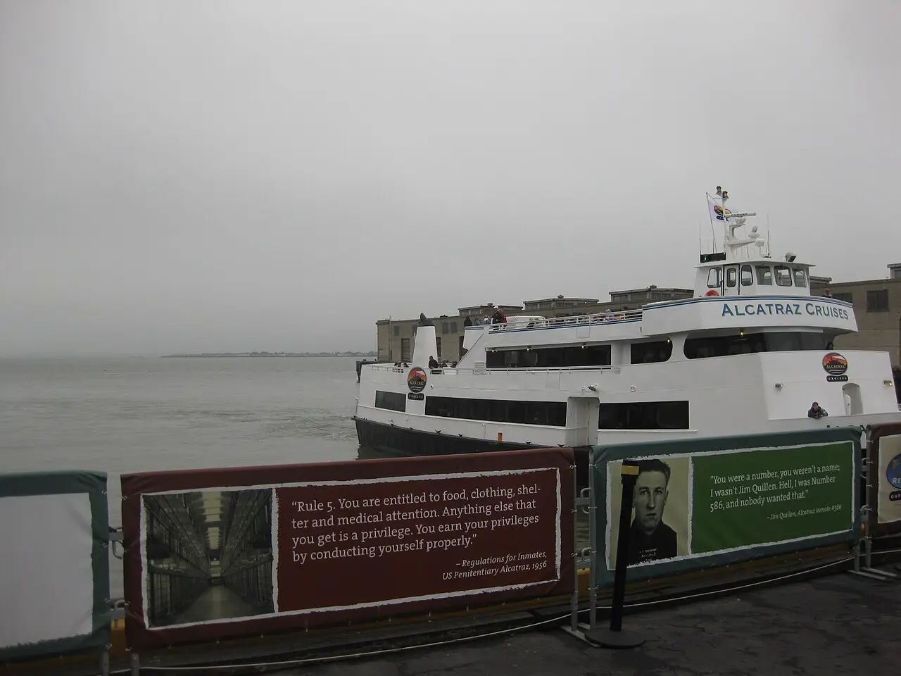 An Alcatraz Cruises ferry docked at Pier 33 with informational signage about prison rules on the railing