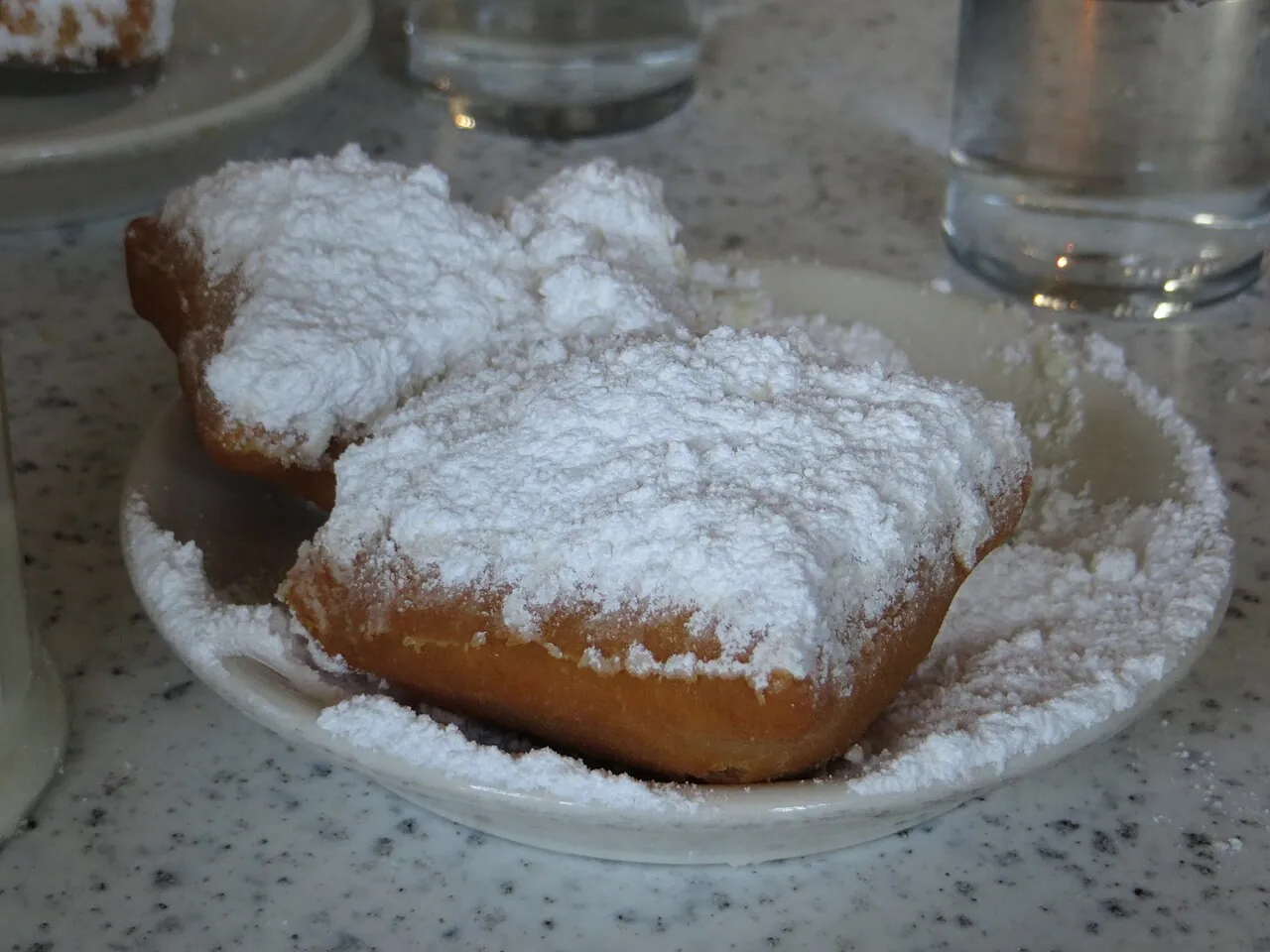 Three beignets under a thick layer of powdered sugar on a plate at Cafe du Monde