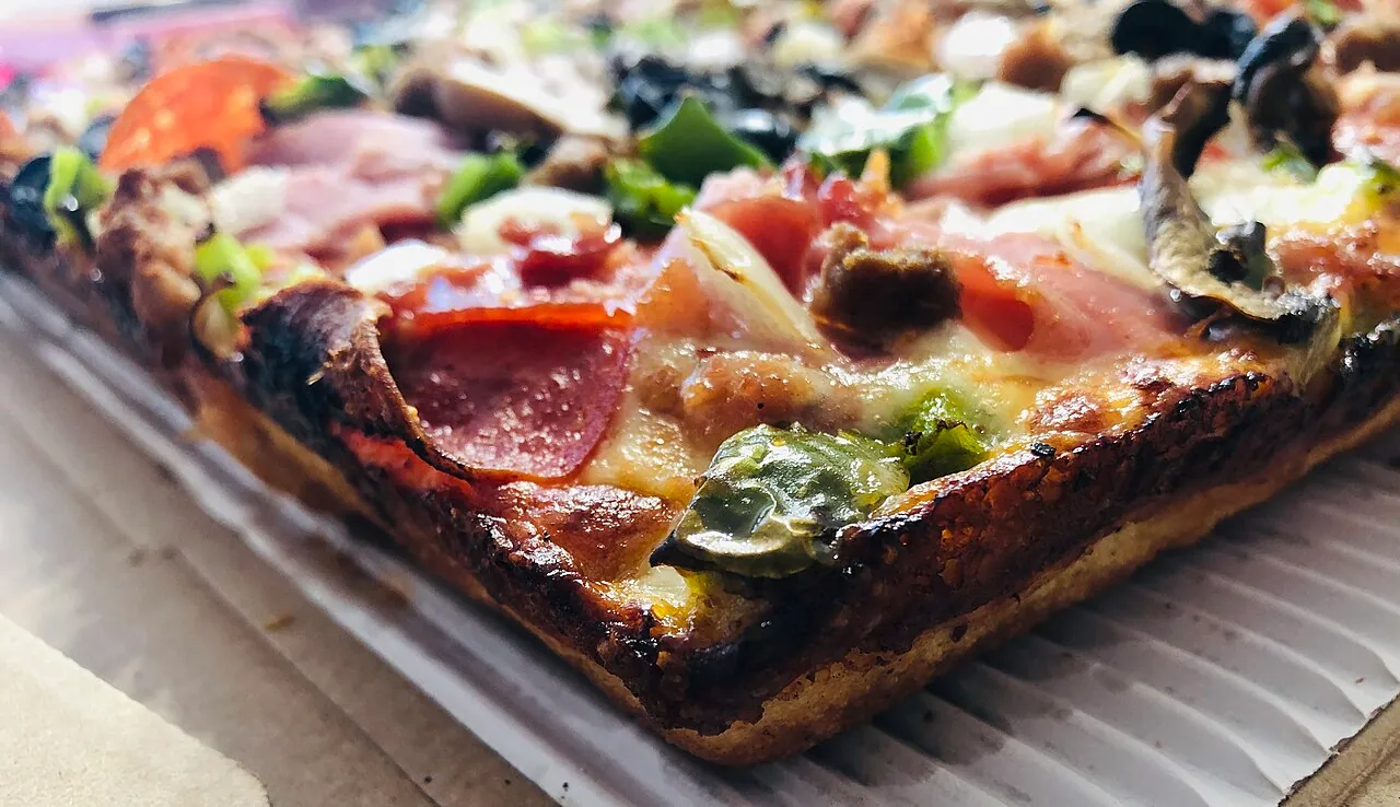 A corner piece of Detroit-style square pizza with a caramelized cheese edge