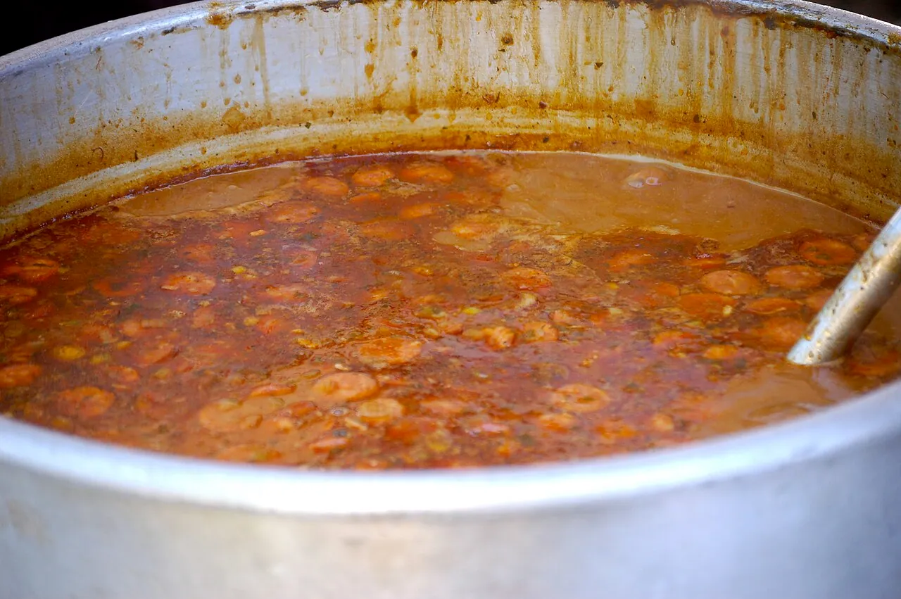A large pot of dark Louisiana gumbo being stirred with a wooden spoon