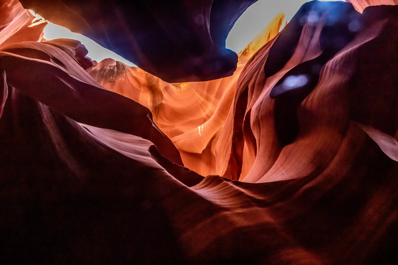 Layered orange and purple sandstone curves lit from a narrow opening above in Lower Antelope Canyon