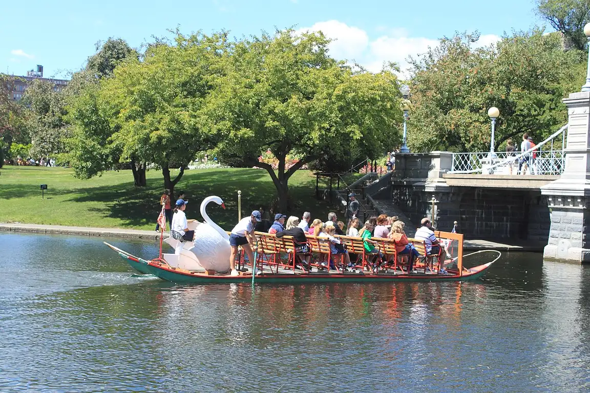 A swan boat passing under the small suspension bridge on the lagoon in Boston Public Garden
