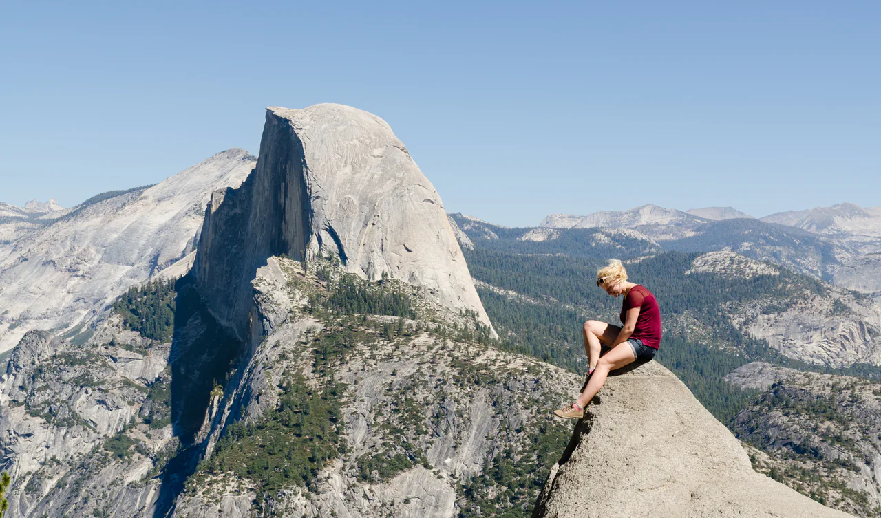 A visitor at the Glacier Point railing in Yosemite with Half Dome rising behind