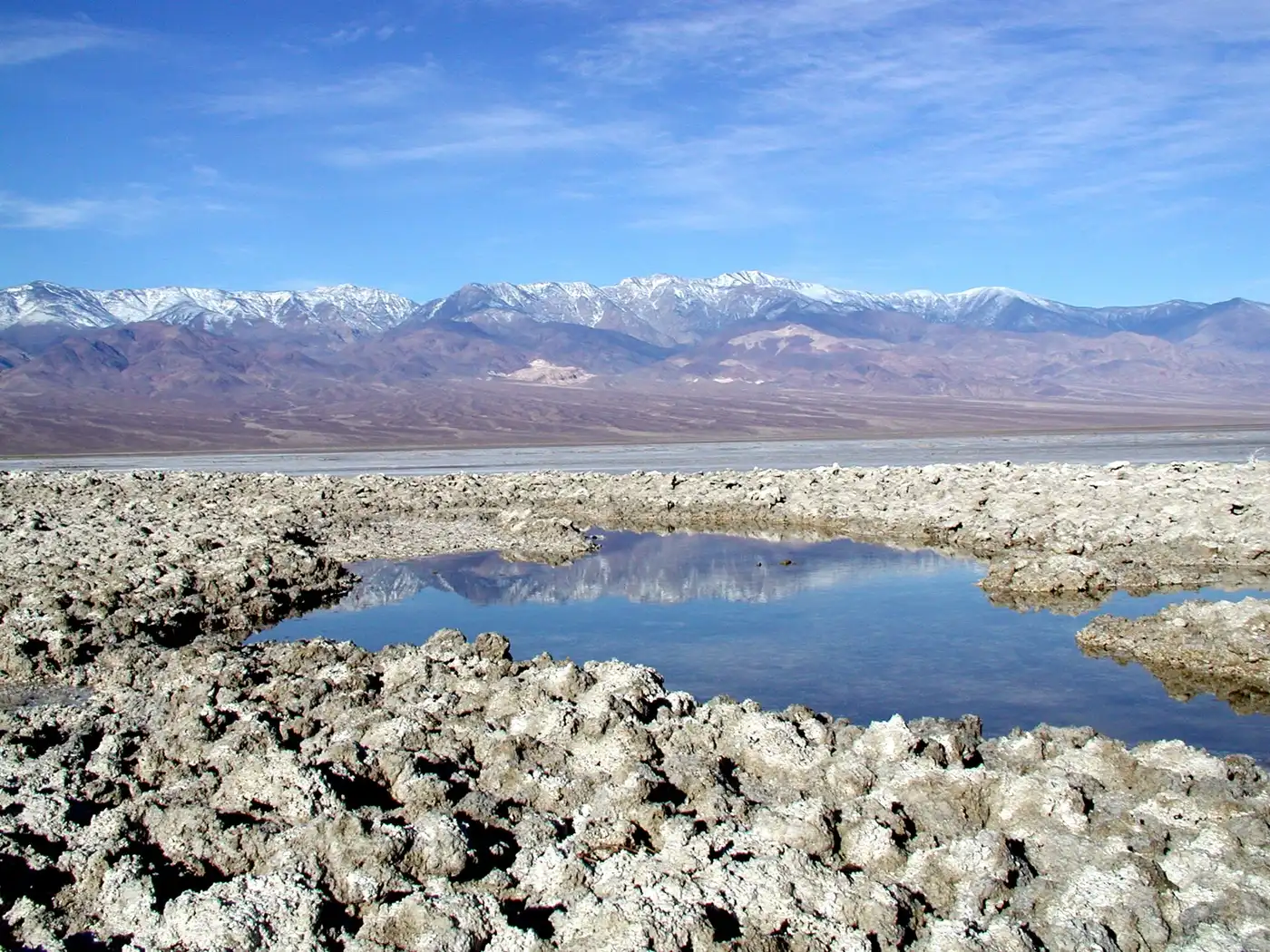 A reflective shallow pool surrounded by a white salt crust in Death Valley