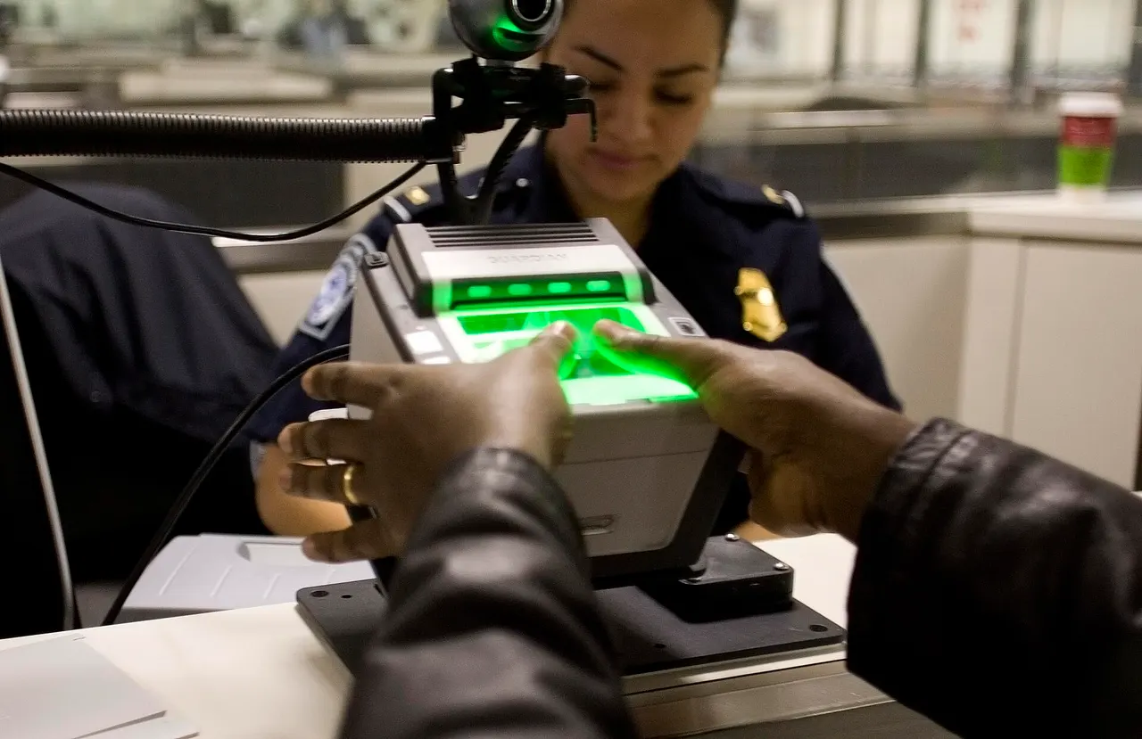 A traveler placing fingers on a glowing green fingerprint scanner in front of a seated CBP officer