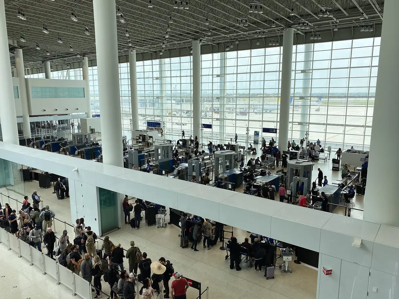 Travelers waiting in a long snaking line at a multi-lane airport security checkpoint
