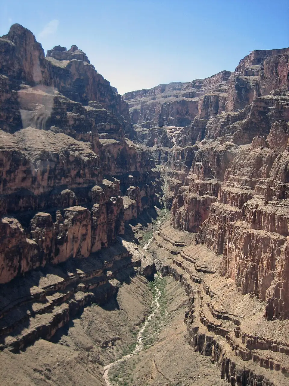 A narrow side canyon with a dry wash, seen through a tour helicopter window