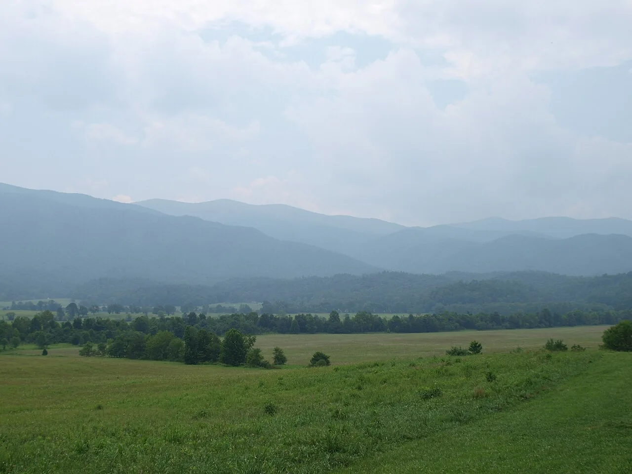Open green meadow of Cades Cove ringed by forested ridges of the Great Smoky Mountains