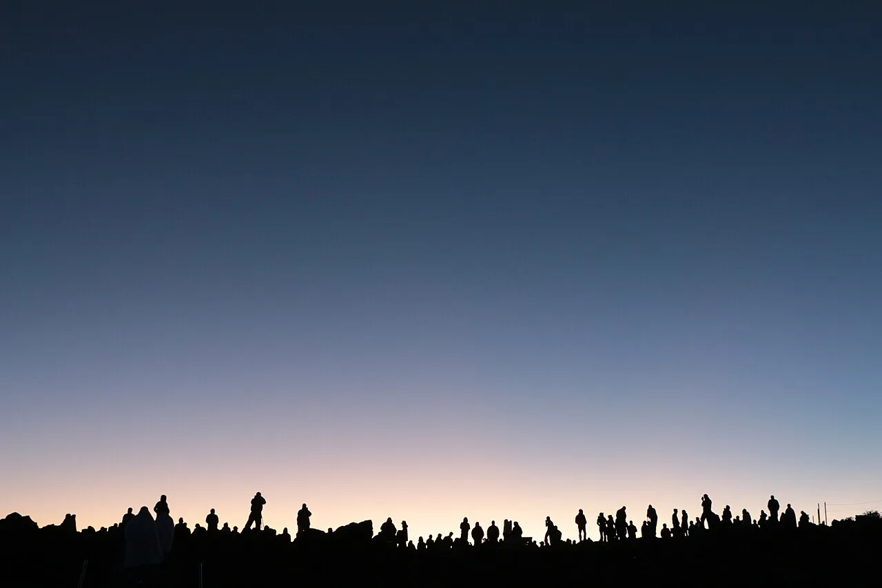 Silhouettes of visitors watching dawn from the Haleakala summit rim above the crater