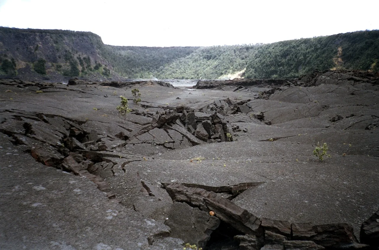 Hikers crossing the black lava floor of Kilauea Iki crater with steep walls around them