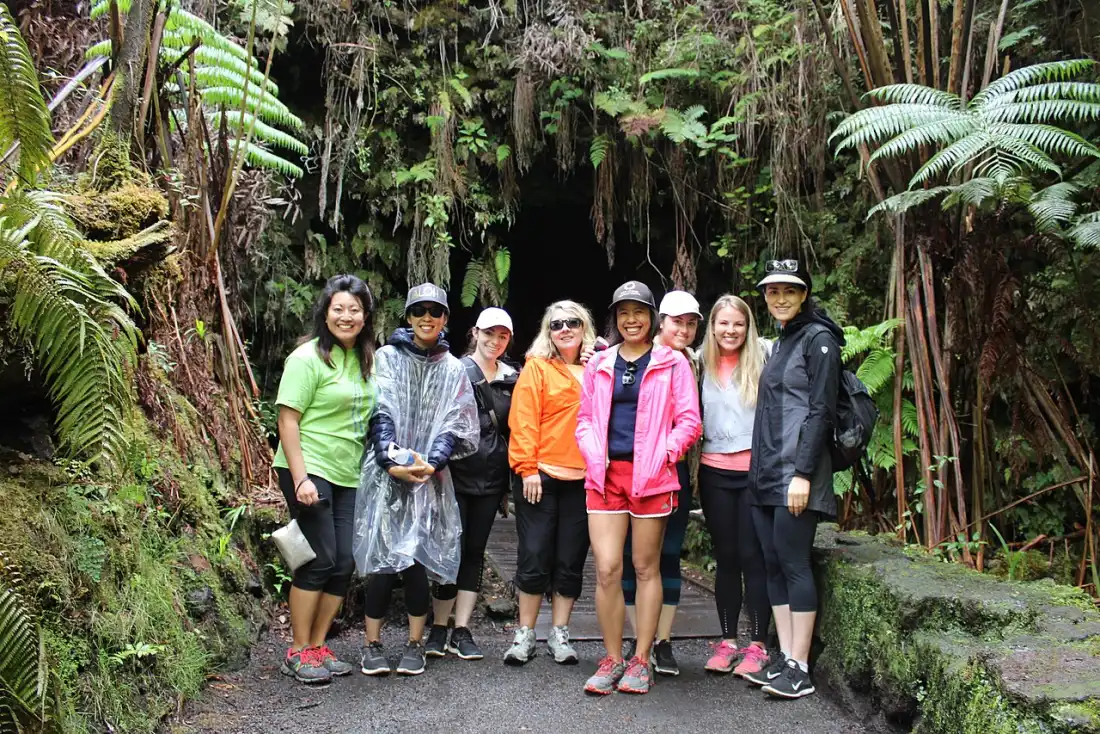 Visitors walking through the lit section of Nahuku Thurston Lava Tube under a fern canopy entrance