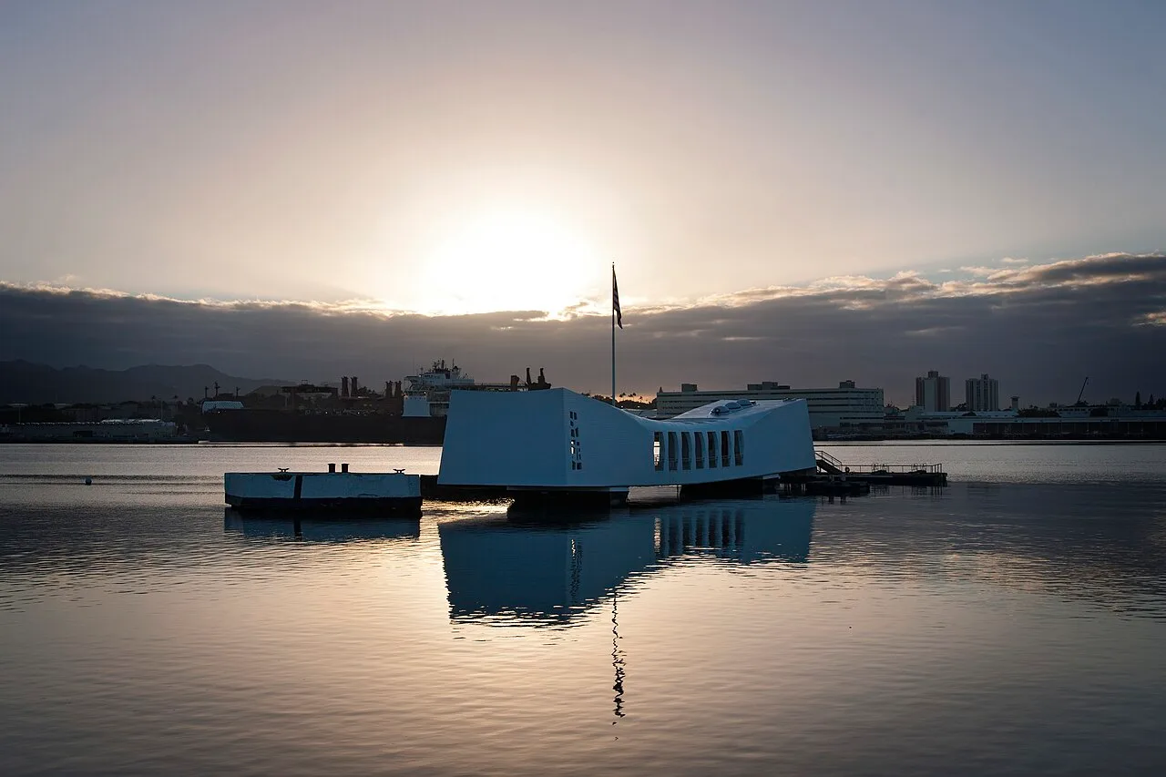 The white USS Arizona Memorial spanning the sunken battleship in Pearl Harbor at sunset