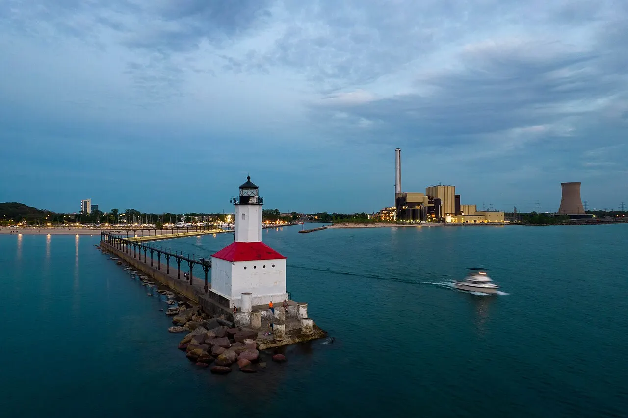 Michigan City East Pier lighthouse on Lake Michigan at dusk with industrial skyline beyond