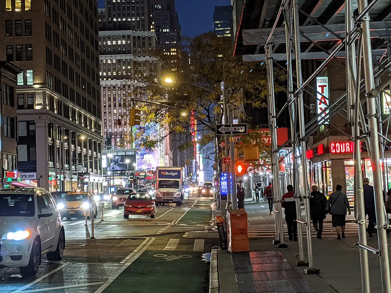 A Manhattan street at dusk with pedestrians and storefronts along Seventh Avenue