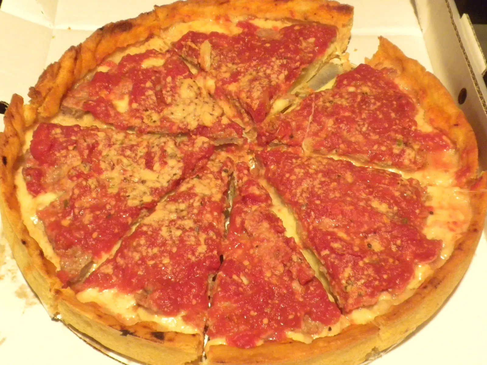 A whole Chicago deep-dish pizza cut into wedges, showing the thick crust and chunky tomato sauce spooned on top
