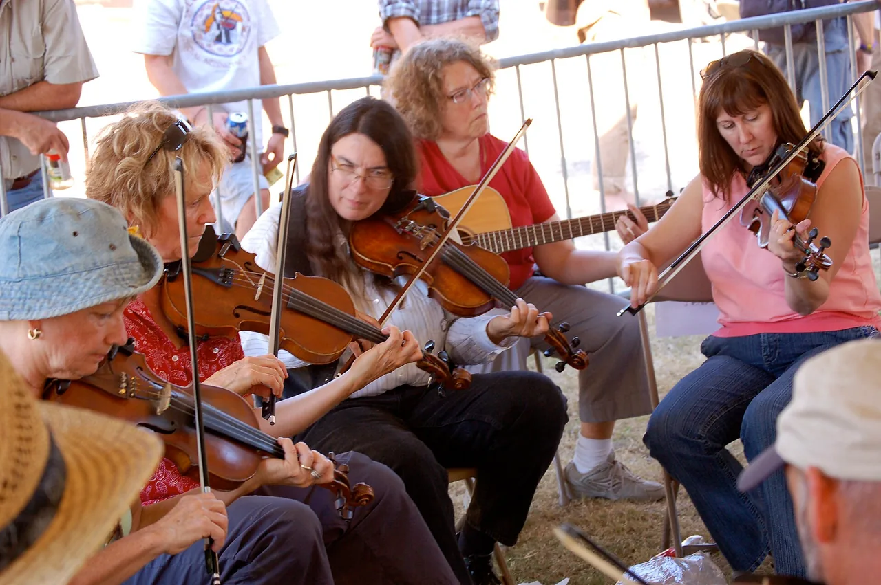 Musicians playing fiddles and guitar together at an open-air Cajun jam session in Louisiana