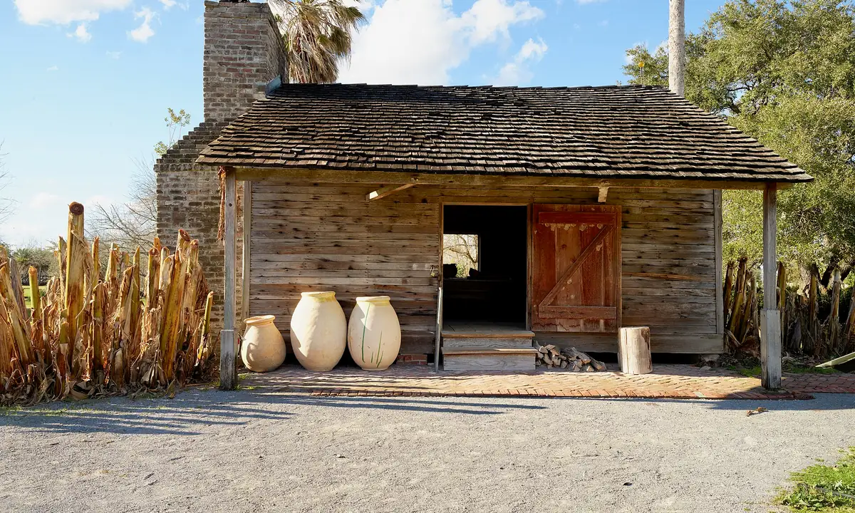 A restored wooden detached kitchen with a brick chimney and clay jars at Whitney Plantation in Wallace, Louisiana