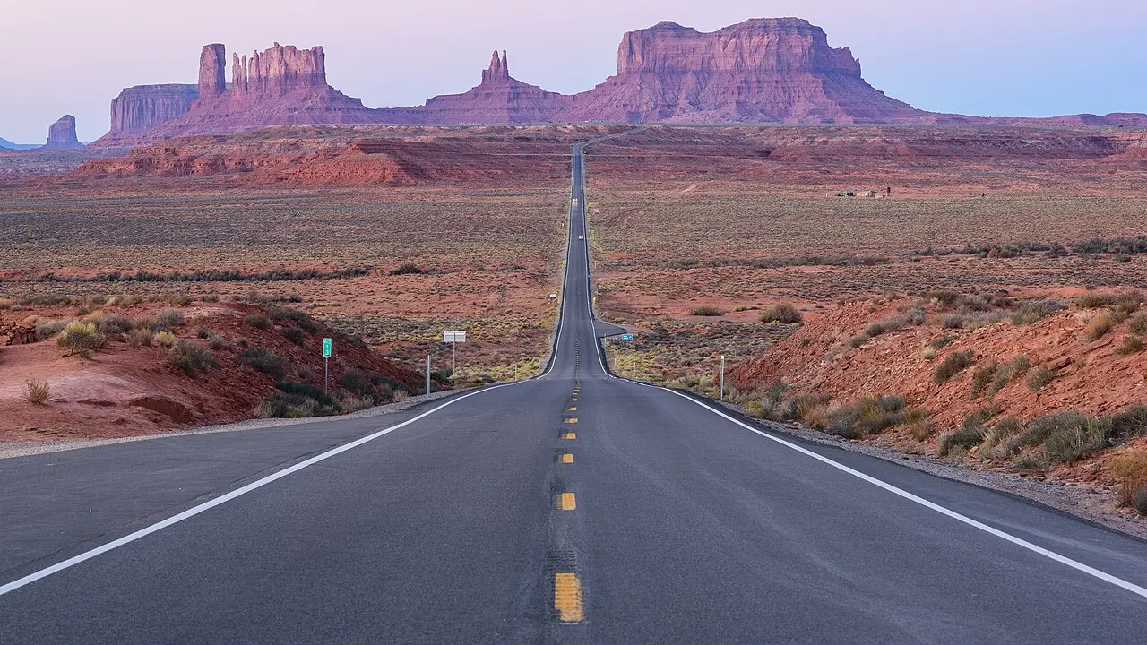 The road at Forrest Gump Point on US-163 running straight toward the buttes of Monument Valley at dawn