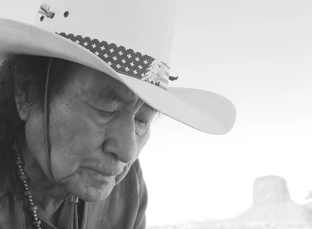 Portrait of a Navajo elder in a wide-brimmed hat at Monument Valley, a butte visible in the background