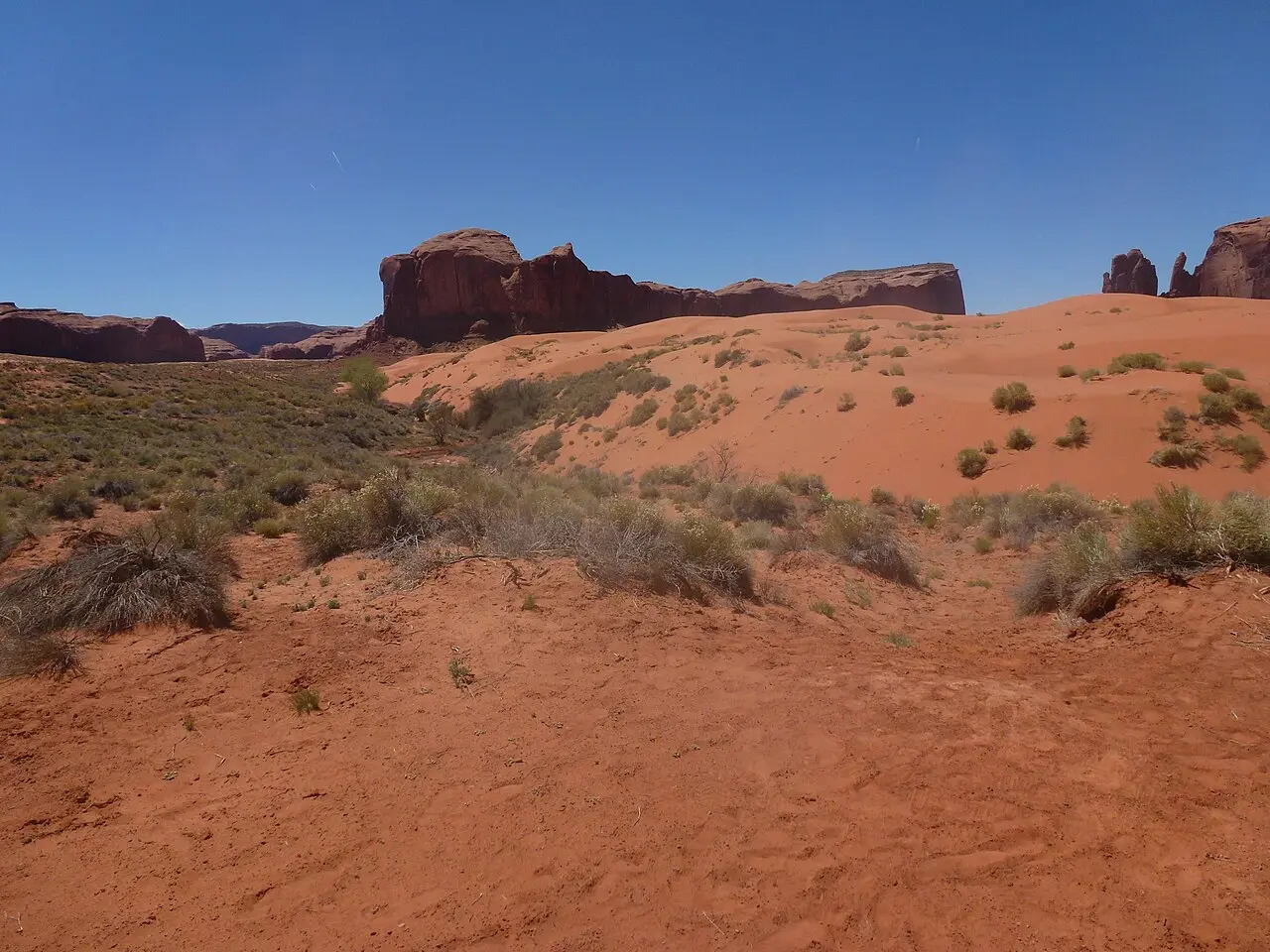 The sandy, rutted valley floor of Monument Valley with distant buttes, showing the rough terrain of the self-drive loop