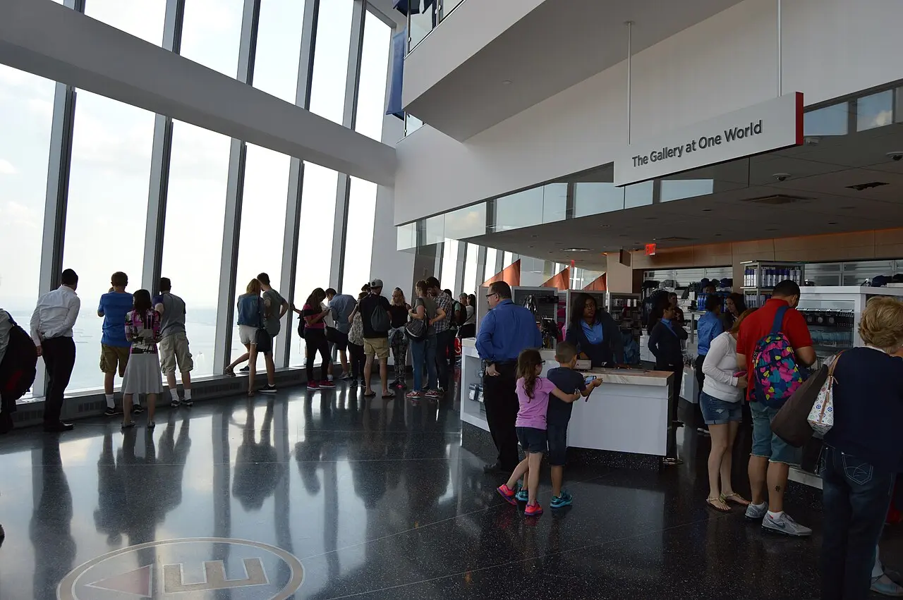 Visitors at the floor-to-ceiling windows inside One World Observatory with a gift shop visible behind them