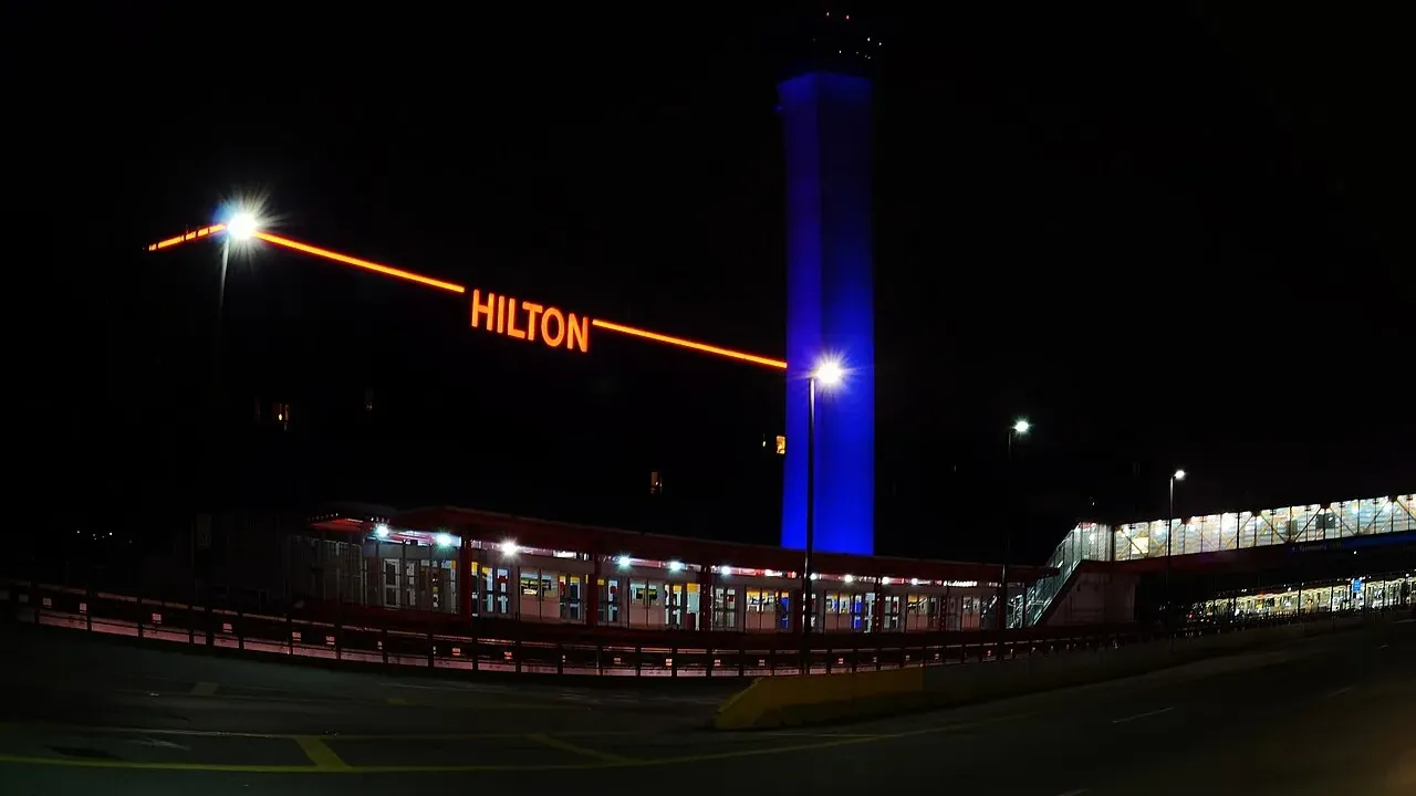 The blue-lit control tower and Hilton sign at Chicago O'Hare at night, with the airport transit structure and terminal lights below