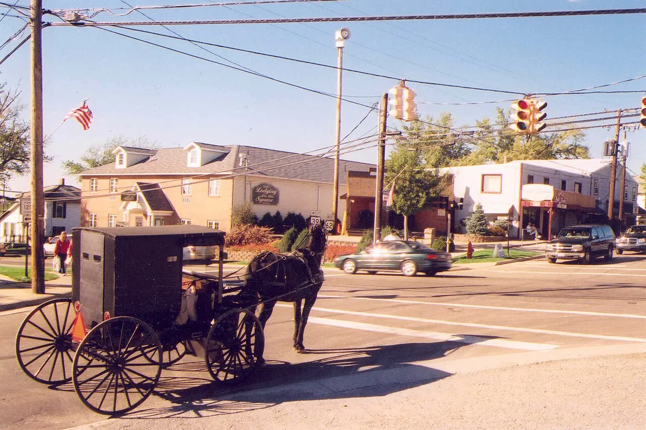 An Amish buggy waiting at a traffic light next to cars at a small-town intersection in Ohio
