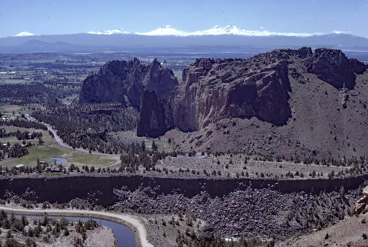 The tan cliffs of Smith Rock above the Crooked River with the snowy Cascade peaks on the horizon