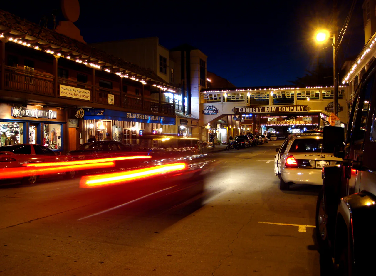Lit storefronts and the old cannery buildings along Cannery Row in Monterey at dusk