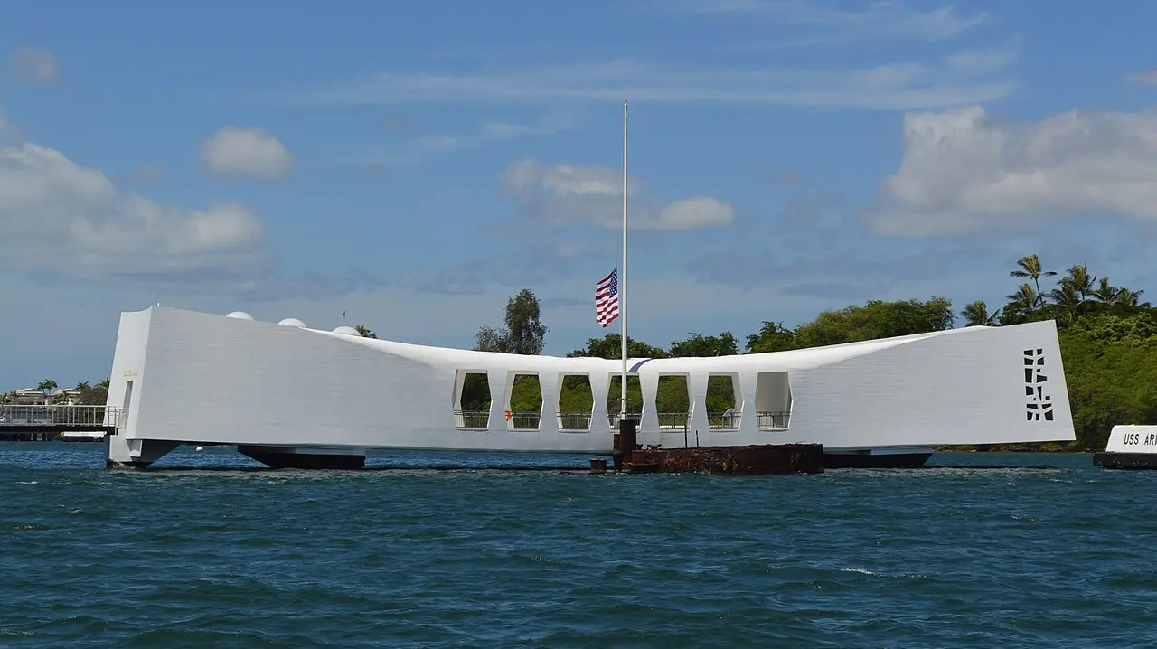 White USS Arizona Memorial spanning Pearl Harbor with the American flag flying above the sunken battleship