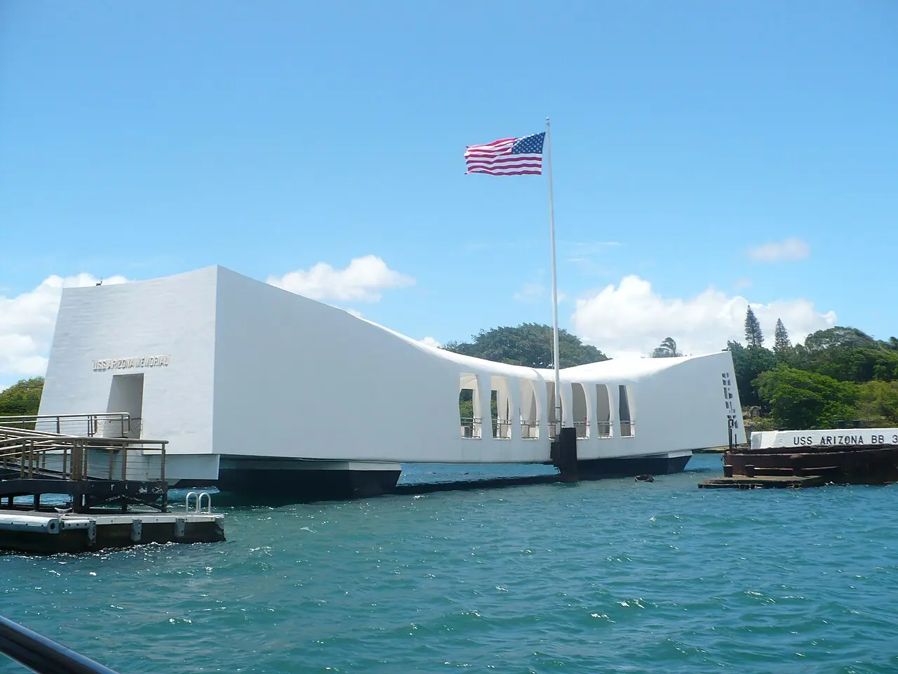 USS Arizona Memorial white structure over turquoise harbor water with Ford Island trees behind