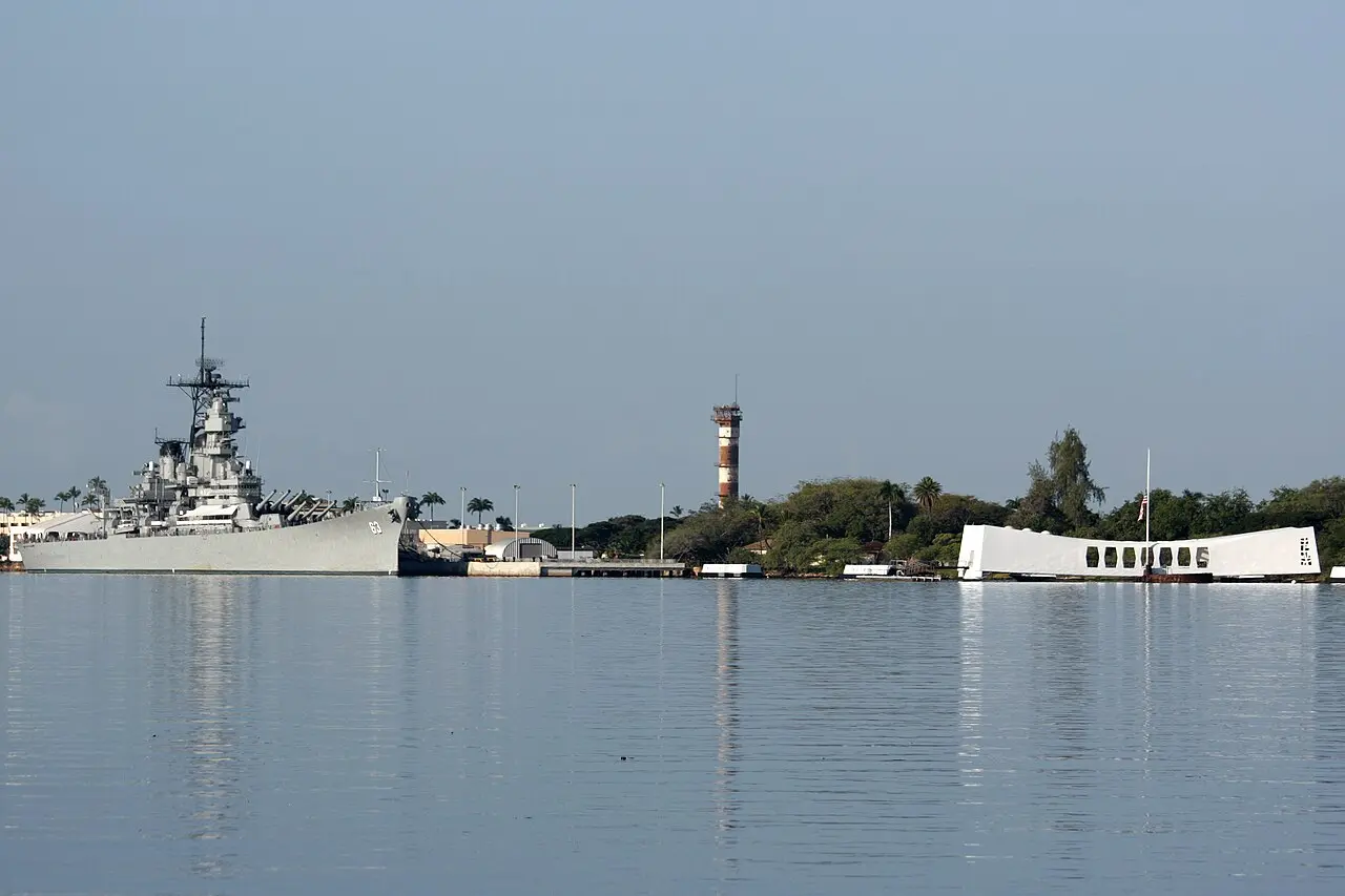 Gray USS Missouri battleship docked near the white USS Arizona Memorial across Pearl Harbor