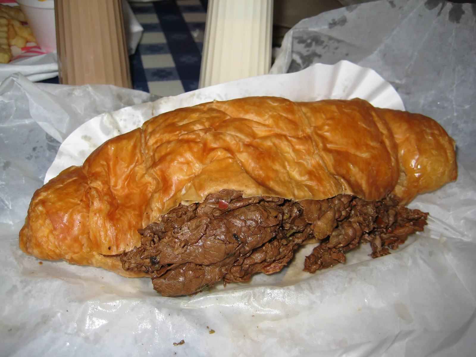 A hand holding a flaky Italian beef sandwich dripping with gravy, sliced open to show the layers of beef