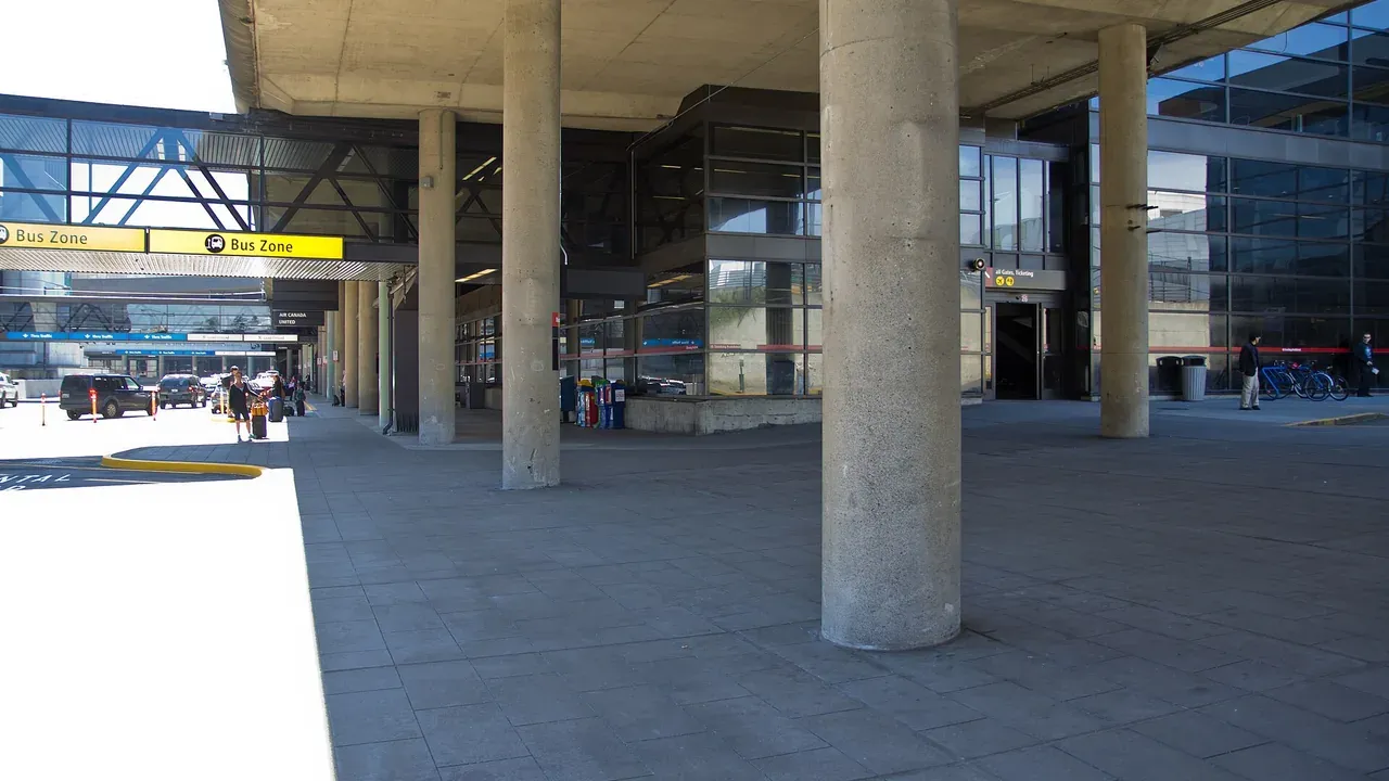 Travelers waiting at a rental car shuttle stop outside an airport