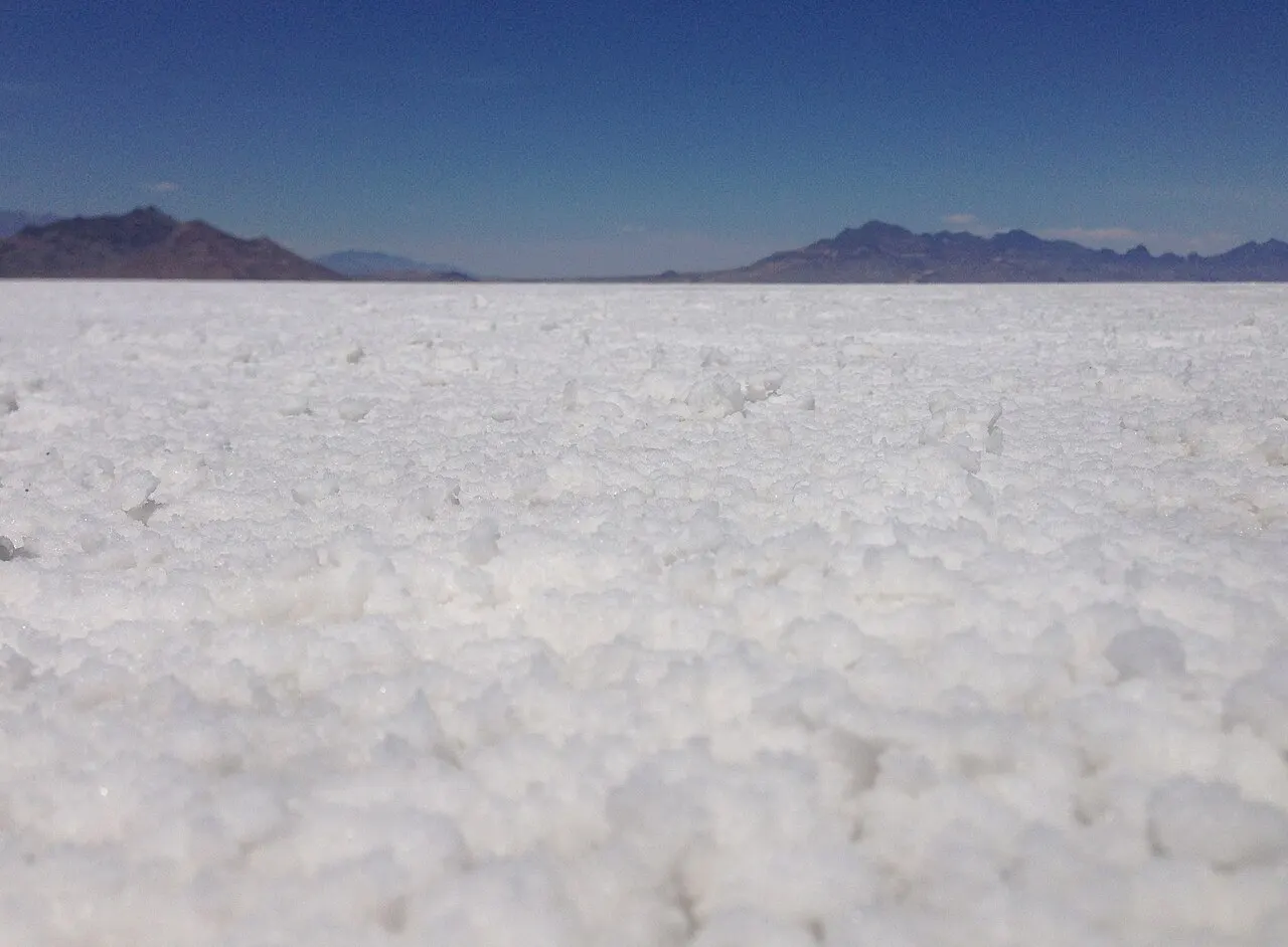 Close-up view of white salt crystals stretching to distant mountains under a deep blue sky at the Bonneville Salt Flats