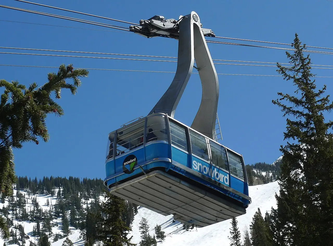 The Snowbird aerial tram cabin suspended against a blue sky with snow-covered peaks below