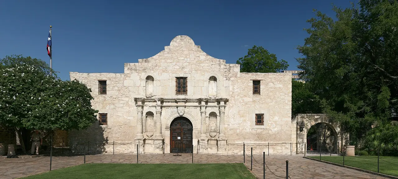 The limestone facade of the Alamo church with the Texas flag flying beside it