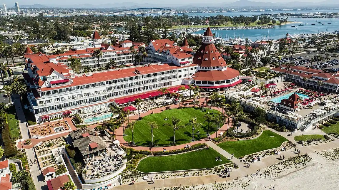 The red-roofed Victorian Hotel del Coronado seen from above with its lawn and the Pacific behind
