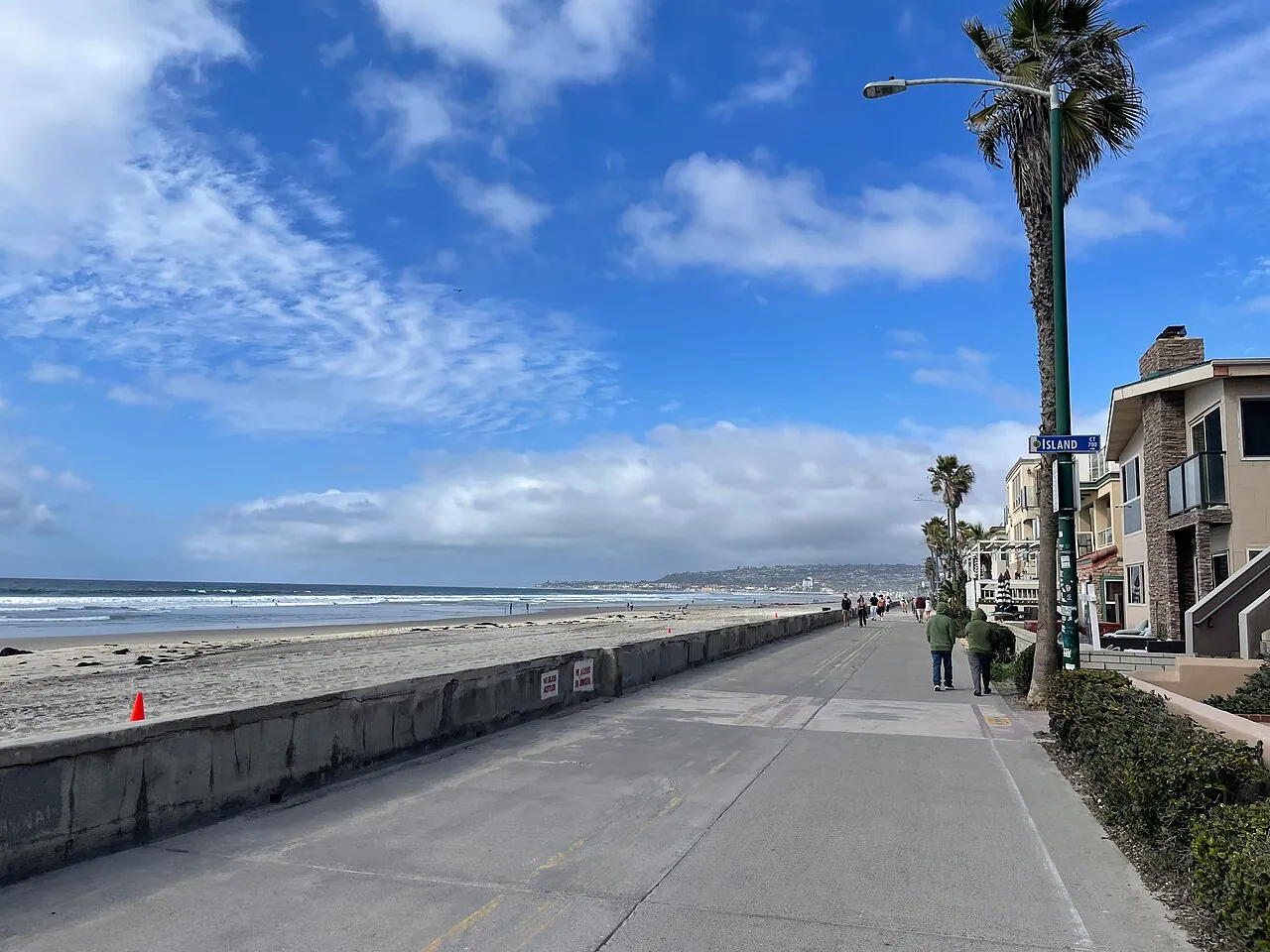 The Mission Beach boardwalk with cyclists and beachfront houses on a sunny day