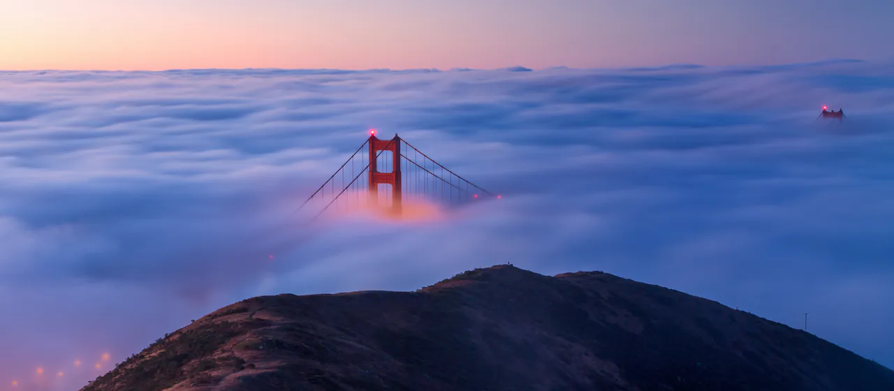 The Golden Gate Bridge towers rising through low fog seen from the Marin Headlands at sunrise
