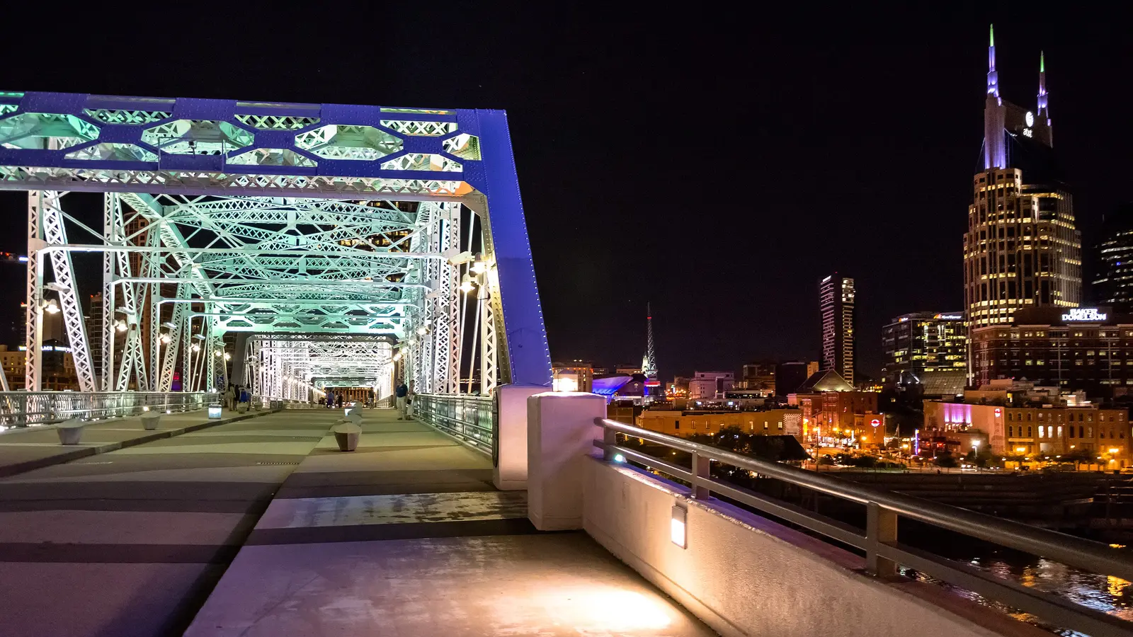 The lit pedestrian bridge over the Cumberland River with the downtown Nashville skyline at night