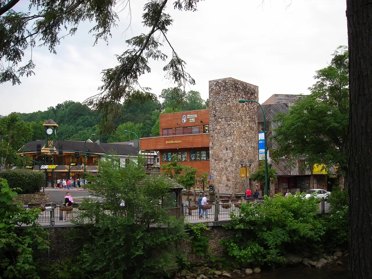 Shops and a stone clock tower along the main street of Gatlinburg beside a mountain creek
