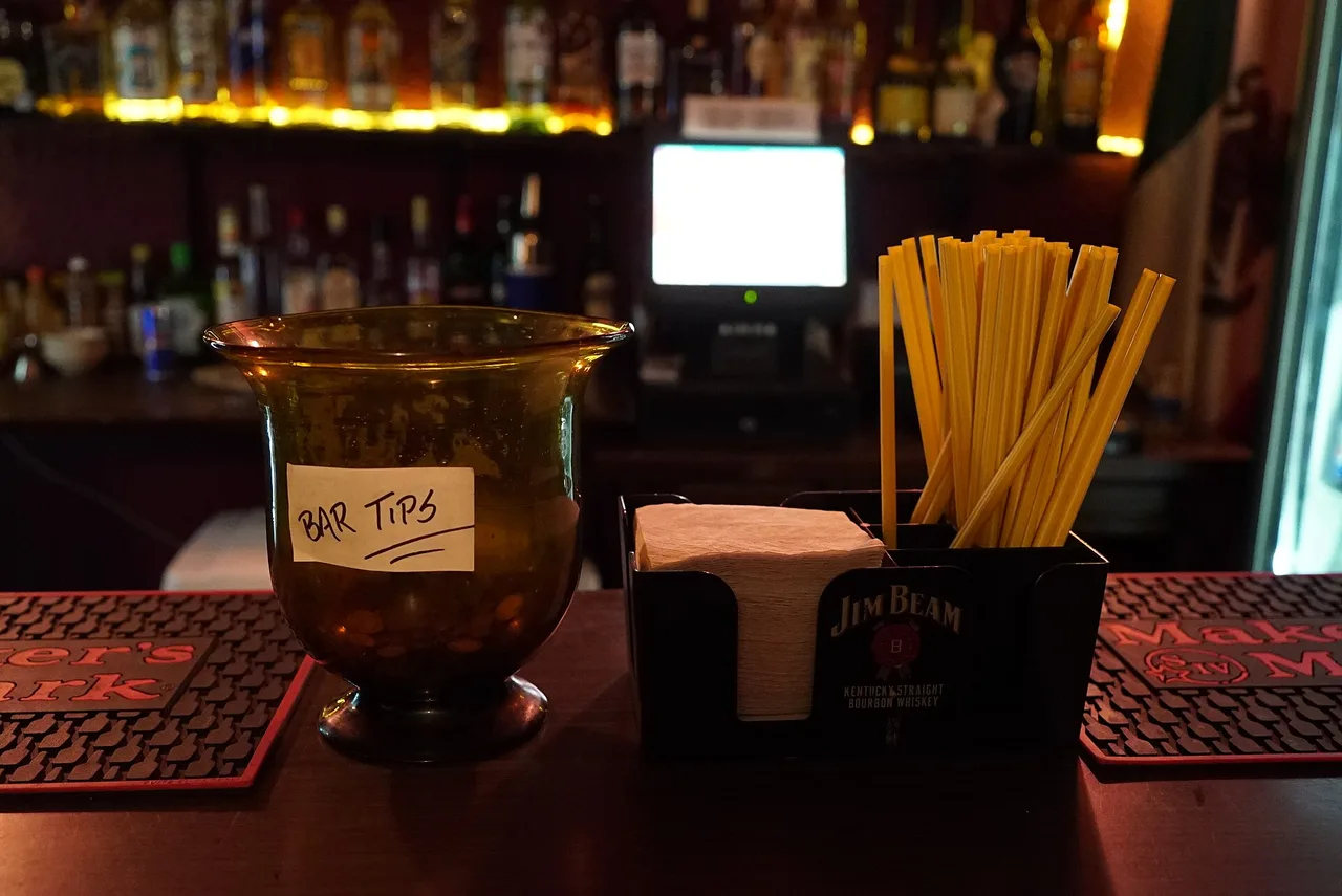 A glass tip jar on a bar counter next to a napkin holder