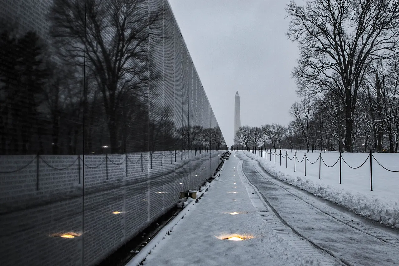 The black granite wall of the Vietnam Veterans Memorial with the Washington Monument behind