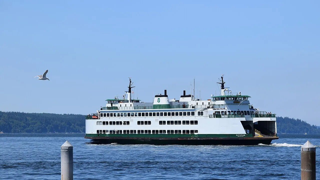 A white and green Washington State ferry crossing Puget Sound with forested shoreline behind