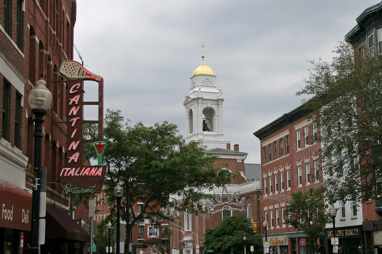 Neon restaurant sign on Hanover Street in Boston's North End with a white church tower behind