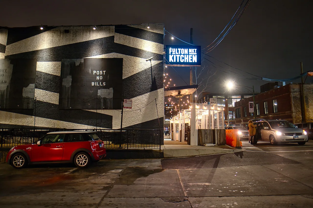 The lit Fulton Market Kitchen sign and a mural on a West Loop street at night
