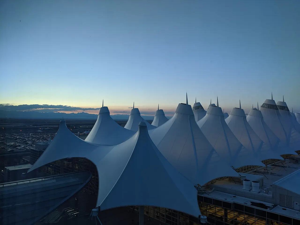 The peaked white tent roof of Denver International Airport at dusk with the Front Range on the horizon