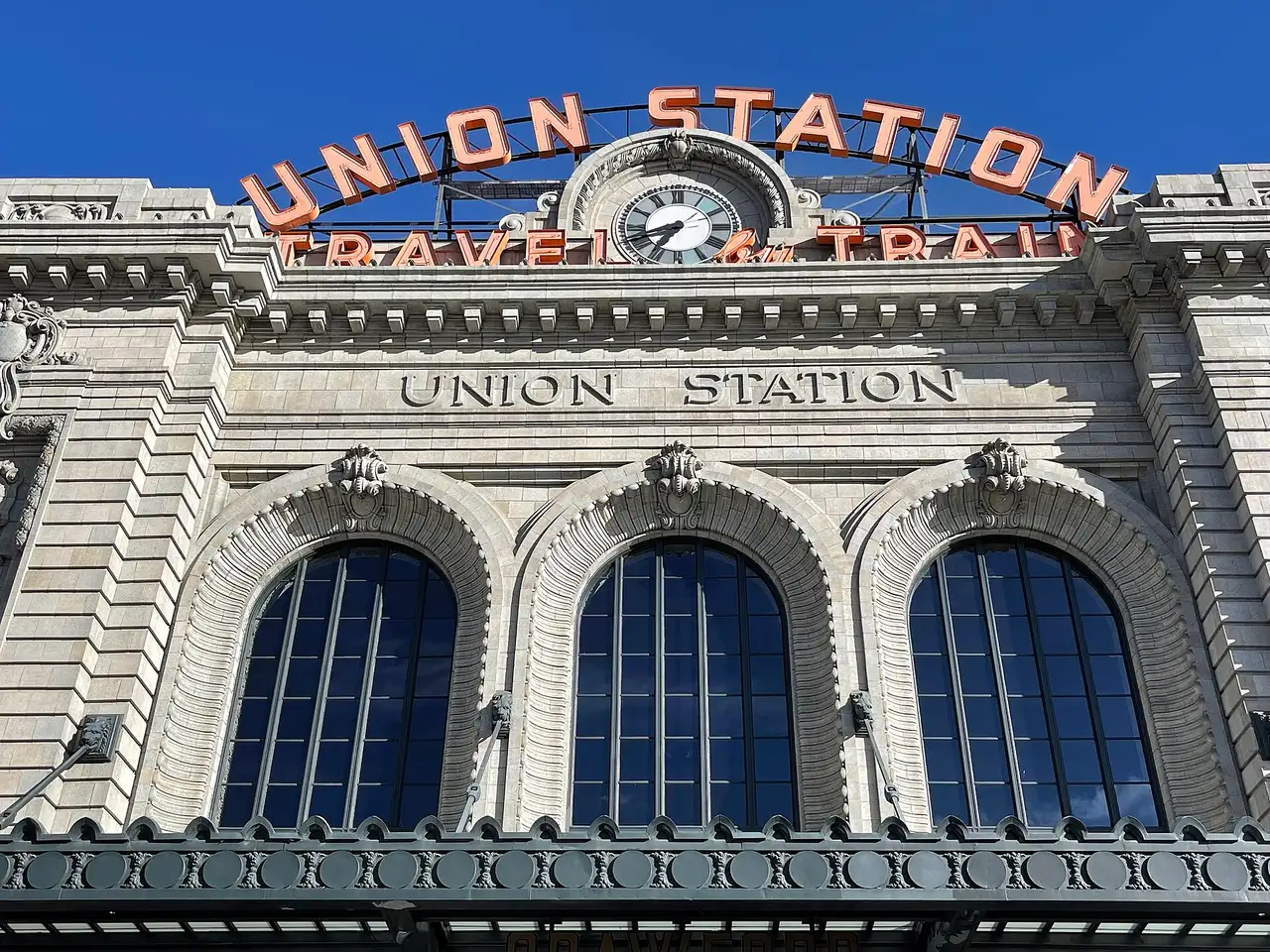 The Union Station neon sign and Travel by Train lettering on the stone facade against a blue sky